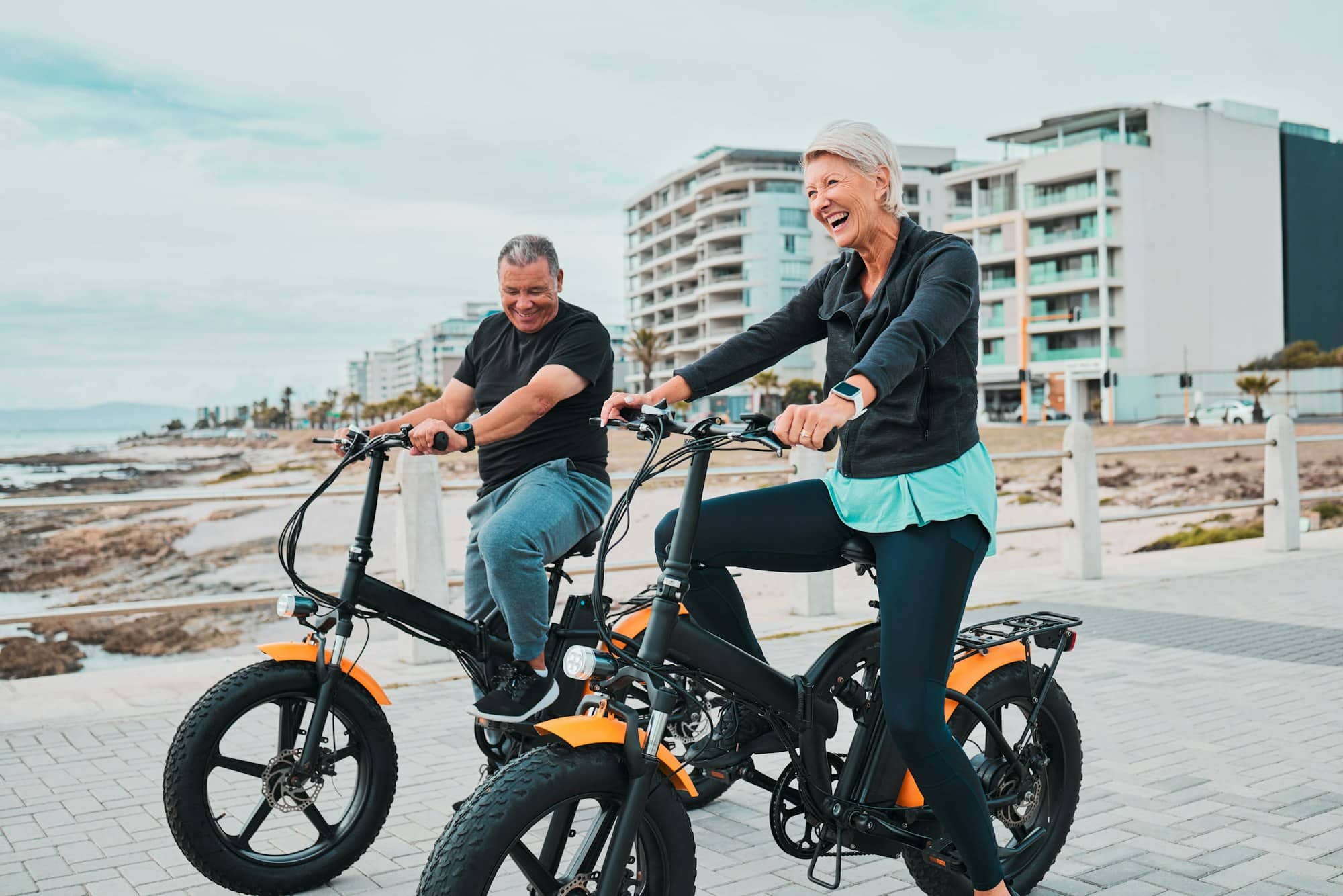 Senior couple, electric bike and smile by the beach for fun bonding cycling or travel together in t